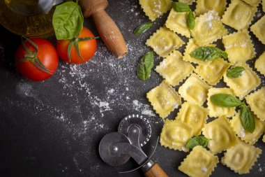 Delicious raw ravioli with flour and basil on dark background. The process of making Italian ravioli.