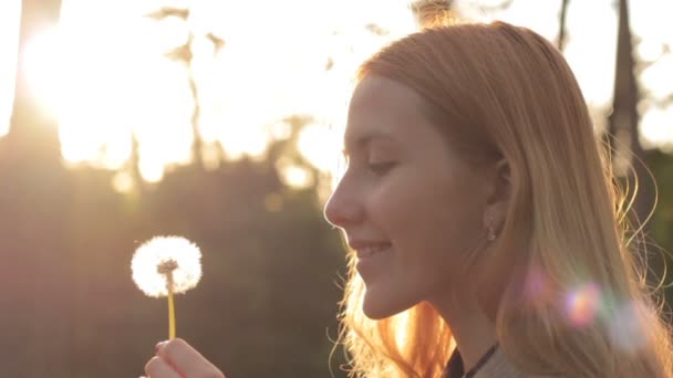 Vue latérale de la fille blonde soufflant sur le pissenlit — Video