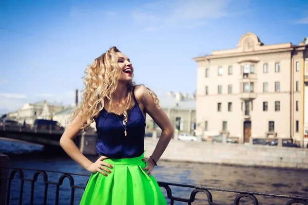 Mooie blonde meisje lachen en poseren tegen de achtergrond van de stad — Stockfoto