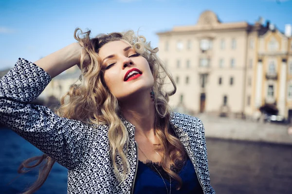 Mooie blonde meisje lachen en poseren tegen de achtergrond van de stad — Stockfoto