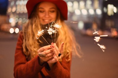 Boş bir şehir, kırmızı şapkalı güzel bir kız, Noel arifesinde ve yılbaşı arifesinde elinde maytaplarla parlayan bir şehrin arka planında.