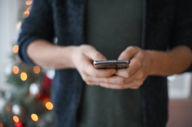 Noel günü, elinde telefon akıllı telefonu olan kot pantolonlu bir adamın elleri yakın plan çekimde.