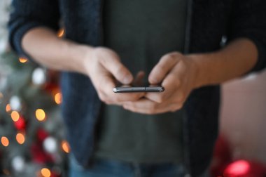 Noel günü, elinde telefon akıllı telefonu olan kot pantolonlu bir adamın elleri yakın plan çekimde.