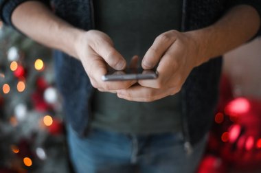 Noel günü, elinde telefon akıllı telefonu olan kot pantolonlu bir adamın elleri yakın plan çekimde.