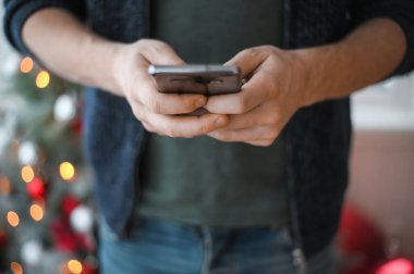 Noel günü, elinde telefon akıllı telefonu olan kot pantolonlu bir adamın elleri yakın plan çekimde.