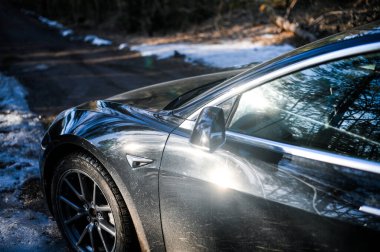 Tonsberg, Norveç - 18 Mart 2021: siyah Tesla modeli 3 Long Range çift motorlu arka planda İskandinav ormanı olan elektrikli bir otomobil..