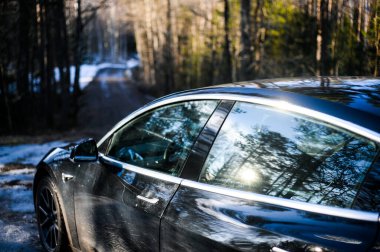 Tonsberg, Norveç - 18 Mart 2021: siyah Tesla modeli 3 Long Range çift motorlu arka planda İskandinav ormanı olan elektrikli bir otomobil..