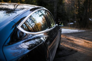 Tonsberg, Norveç - 18 Mart 2021: siyah Tesla modeli 3 Long Range çift motorlu arka planda İskandinav ormanı olan elektrikli bir otomobil..