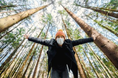 Uzun kollu siyah ceket ve gözlüklü turuncu şapkalı çekici inek portresi. Gün batımında çam ormanında koruyucu yüz maskesi.