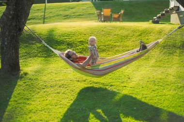 Parktaki yeşil çimenli gözlüklü çekici inek portresi hamağın yanında erkek bir bebekle günbatımını güzel bir şekilde geçirin. Mutlu babalar