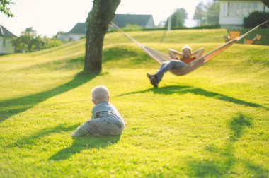 Parktaki yeşil çimenli gözlüklü çekici inek portresi hamağın yanında erkek bir bebekle günbatımını güzel bir şekilde geçirin. Mutlu babalar