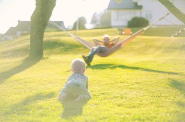 Parktaki yeşil çimenli gözlüklü çekici inek portresi hamağın yanında erkek bir bebekle günbatımını güzel bir şekilde geçirin. Mutlu babalar