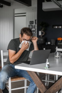 Gözlüklü, çekici, inek bir adam. Covid salgını veya grip sırasında evden çalışıyor.