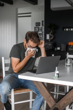 Gözlüklü, çekici, inek bir adam. Covid salgını veya grip sırasında evden çalışıyor.