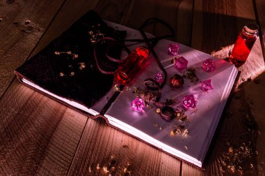 Pink and red role playing dice on top of a leather bound notepad. Two glass bottles with red liquid on a wooden table clipart