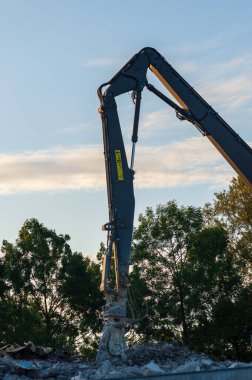 Kudretli Yıkım Kazıcısı, beton eziciyle gün batımında çekilmiş.