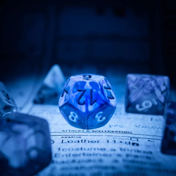 Transparent poly dice D12 illuminated from below with soft blue light on a dungeons and dragons character sheet.