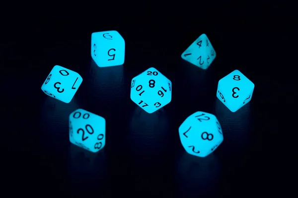 Set of polyhedral luminescence role playing dice glowing in the dark on a black surface