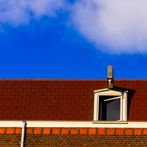Red rooftop with a white atic window against a blue sky