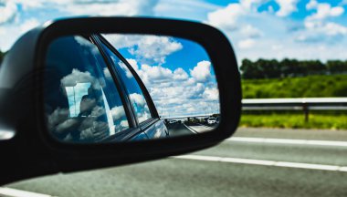 Otobanda siyah bir arabanın aynasında bulutlu bir görüntü.
