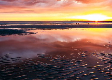 Gün batımında plajda pembe bulutların yansıması.