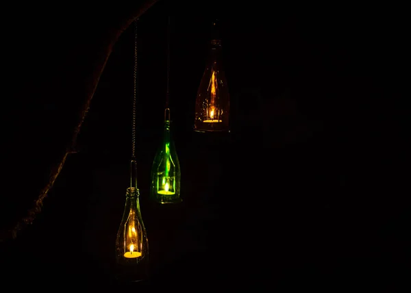 three tea light candles in glass bottles hanging from a tree branch