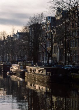 Amsterdam, Hollanda 16 Aralık 2020: Amsterdam 'da kış sonunda parlayan yüzen yüzen yüzen yüzen teknelerin ve sudaki yansımalarının olduğu dikey bir kanal görüntüsü
