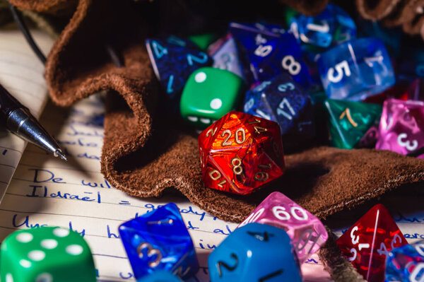Close-up image of role playing dice of various shapes and colors spilling out of a leather dice bag on a open notebook.