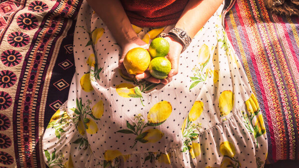 Индонезийская женщина в белом платье с лимонами и горошек сидит на красочном диване с лимоном и двумя лаймами - вертикальное изображение