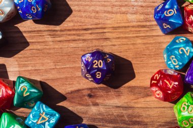 Close-up overhead images of a purple 20-sided die surrounded by various colored and shaped RPG dice on a wooden table in the sunlight clipart