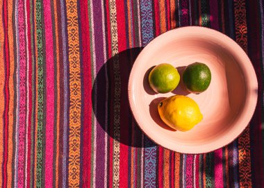 Renkli çizgili bir masa örtüsü üzerinde limon ve limonlu pembe pastel çorba tabağı resmi.