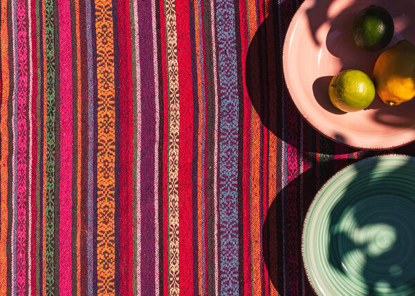 изображение розовых и пастельно-зеленых тарелок супа, двух лимонов и лайма на красочной скатерти на солнечном свете