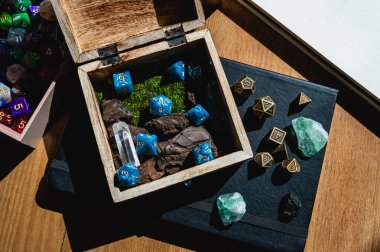 Image of a wooden box with blue role-playing game dice on top of a black notebook with green crystals and metal dice. clipart