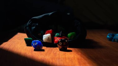 16: 9 yatay görüntü kırmızı ve siyah misketli 20 kenarlı RPG güneş ışığında siyah bir zar çantasının önünde ölüyor.
