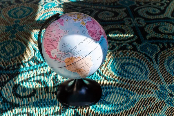 Image of a small world globe on a blue eastern-inspired carpet in the afternoon sun