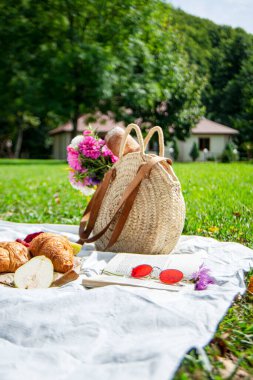 Hasır sepet içinde romantik bir piknik için parktaki beyaz bir battaniye çimenlikte öğle yemeği, sokakta atıştırmalık