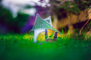 Yeşil taze çimenlerin üzerindeki küçük vitraylı ev, çok renkli camlardan yapılmış el sanatları, yeşil bulanık arka plan