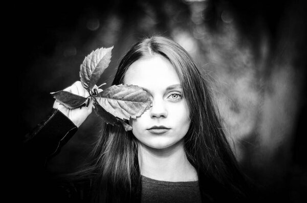 Horizontal portrait of a girl with a leaf, piercing gaze of a young woman, space for text, copy space, black and white defiant portrait