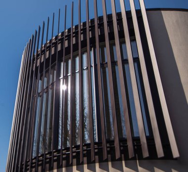 Mavi gökyüzünün altında cam ve çelik yapılardan oluşan modern bir bina. Mimaride paralel çizgiler. Bir binanın parçası, çelik ve camdan yapılmış ofis binası..