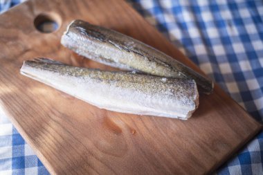 Tahtadaki çiğ balık, sağlıklı vejetaryen yiyecekler, mutfak tahtasındaki donmuş hake (Merluccius), balık pişirme