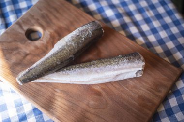 Tahtadaki çiğ balık, sağlıklı vejetaryen yiyecekler, mutfak tahtasındaki donmuş hake (Merluccius), balık pişirme