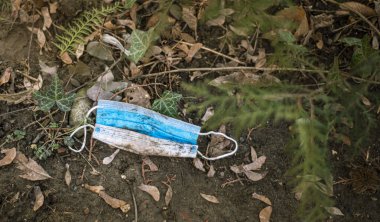 COVID-19 sırasında israf. Yüz kirliliği, çimenlerin üzerindeki çamurla kaplı mavi maske, ilkbaharda koronavirüsün attığı tek kullanımlık yüz maskeleri, ekolojik şehirler ve plastik kirliliği.