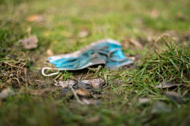 COVID-19 sırasında israf. Yüz kirliliği, çimenlerin üzerindeki çamurla kaplı mavi maske, ilkbaharda koronavirüsün attığı tek kullanımlık yüz maskeleri, ekolojik şehirler ve plastik kirliliği.