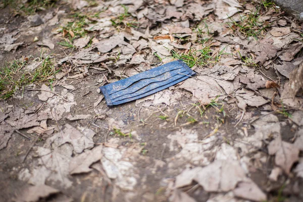 face masks Pollution, blue dirty mask covered in mud in the park on the ground with dry leaves, disposable face masks thrown out by the coronavirus in the spring, anti-epidemiological