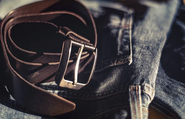 leather belt is a casual wardrobe accessory. Beautiful leather belt and jeans close-up. Men's brutal accessories, belt on a dark background with blurred depth of field, brown belt and denim