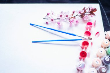 Tüplerdeki boyalar ve beyaz bir tuvaldeki fırçalar, numaralarla yapılmış tablolar, boş bir kağıt ve pembe boyalar, yeni başlayanlar için tablolar ve yakın plan bir tuvaldeki bahar kırmızı çiçekleri, yaratıcılık için bir set. 