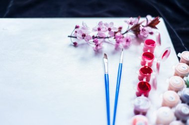 Tüplerdeki boyalar ve beyaz bir tuvaldeki fırçalar, numaralarla yapılmış tablolar, boş bir kağıt ve pembe boyalar, yeni başlayanlar için tablolar ve yakın plan bir tuvaldeki bahar kırmızı çiçekleri, yaratıcılık için bir set. 