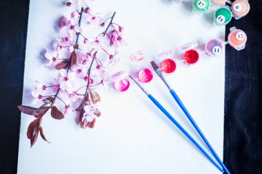 Tüplerdeki boyalar ve beyaz bir tuvaldeki fırçalar, numaralarla yapılmış tablolar, boş bir kağıt ve pembe boyalar, yeni başlayanlar için tablolar ve yakın plan bir tuvaldeki bahar kırmızı çiçekleri, yaratıcılık için bir set. 