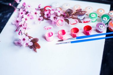 Tüplerdeki boyalar ve beyaz bir tuvaldeki fırçalar, numaralarla yapılmış tablolar, boş bir kağıt ve pembe boyalar, yeni başlayanlar için tablolar ve yakın plan bir tuvaldeki bahar kırmızı çiçekleri, yaratıcılık için bir set. 