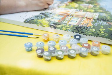 Painting for beginners, a woman draws a picture by numbers with acrylic paints on canvas artist draws a picture, painting a picture with a brush, a girl draws a picture, self-isolation, home hobby